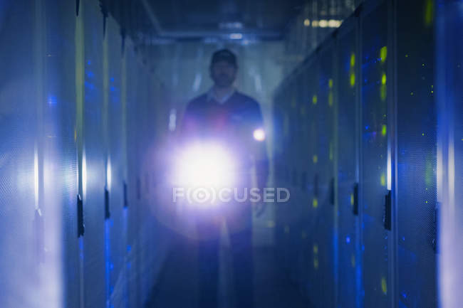 Technicien de salle de serveurs avec lampe de poche dans le couloir sombre — Photo de stock
