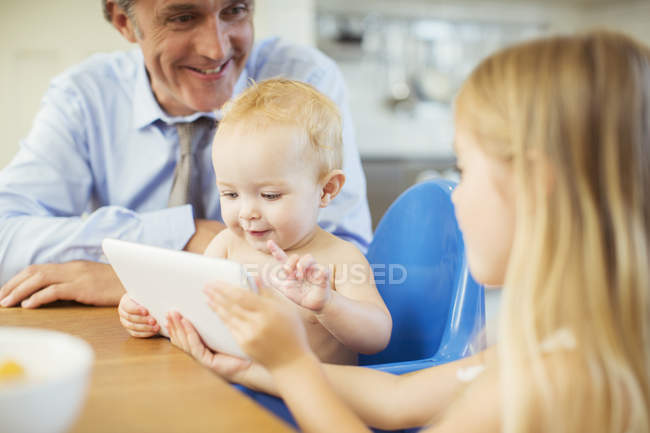 Pai e filhos usando tablet digital à mesa — Fotografia de Stock