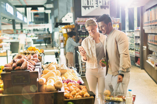 Giovane coppia con cellulare negozio di alimentari al mercato — Foto stock