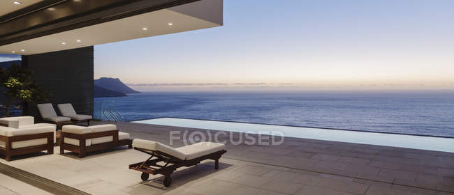 Terrasse moderne et piscine à débordement donnant sur l'océan au coucher du soleil — Photo de stock