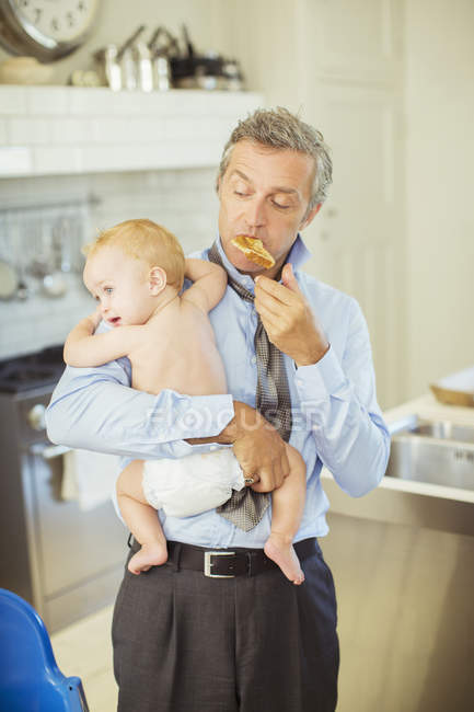 Father holding baby and eating breakfast — Stock Photo