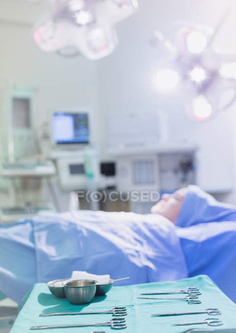 Surgical scissors and equipment on tray near female patient in operating room — Stock Photo