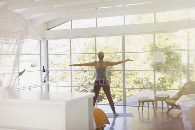 Woman practicing yoga with arms outstretched in sunny modern bedroom — Stock Photo