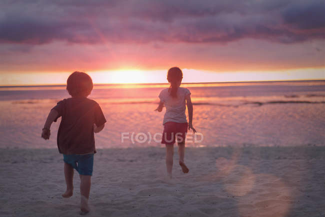 Мальчик и девочка брат и сестра на спокойном пляже заката с драматическим небом — стоковое фото