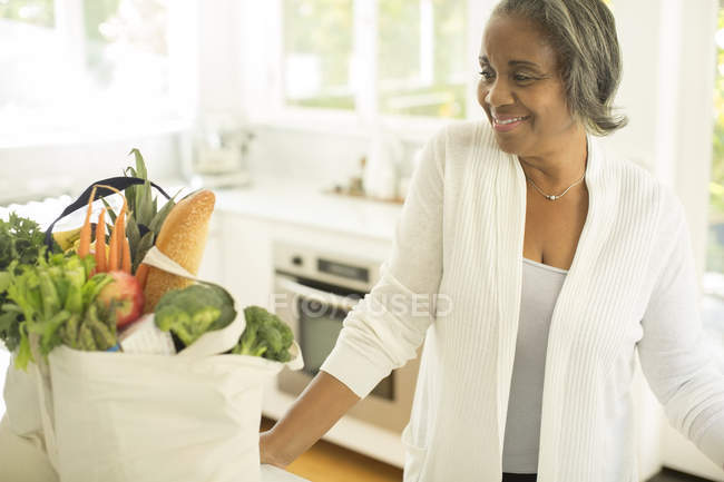 Souriantes femmes âgées avec épicerie dans la cuisine — Photo de stock