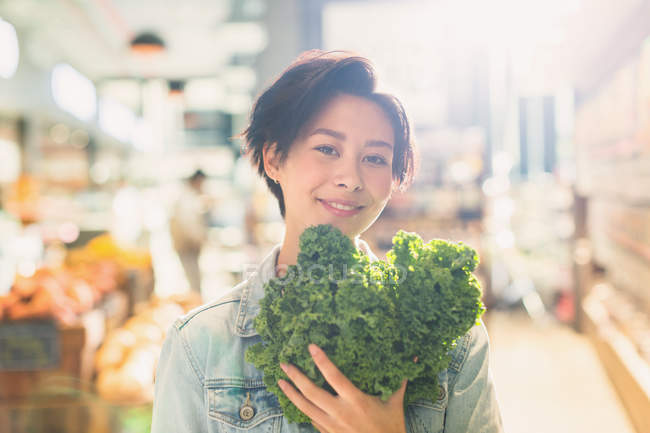 Портрет усміхненої молодої жінки, що тримає свіжу капусту на ринку продуктових магазинів — стокове фото