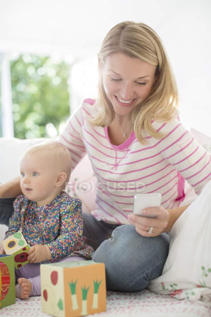 Mãe brincando com bebê menina e verificando o telefone celular — Fotografia de Stock