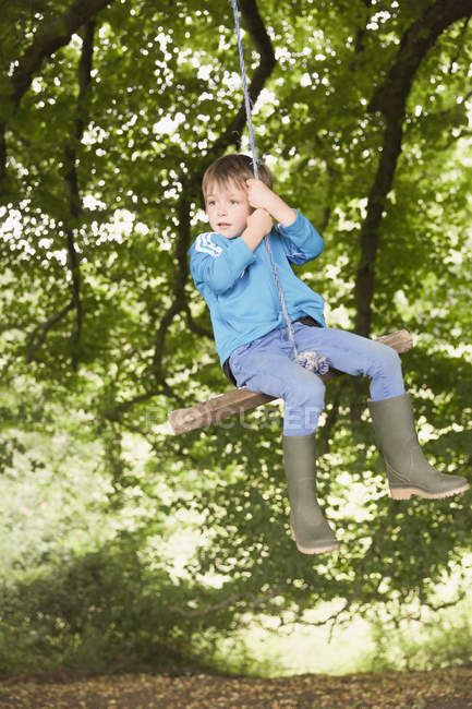 Menino no wellies balançando no árvore corda swing — Fotografia de Stock