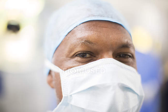 Retrato de médico vestindo tampa cirúrgica e máscara em sala de operações — Fotografia de Stock