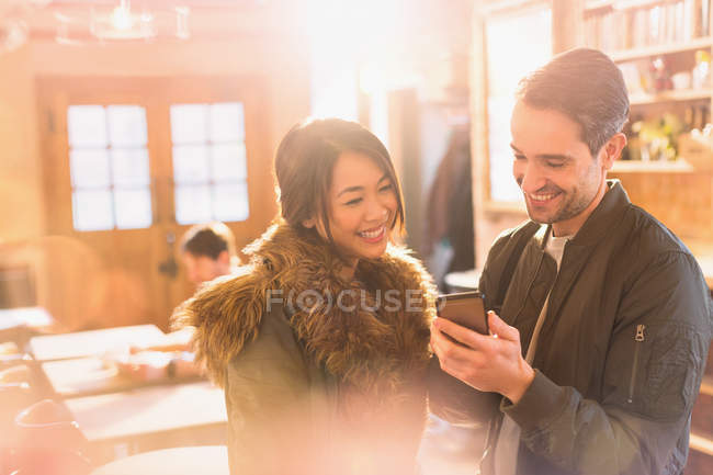 Feliz pareja usando el teléfono celular en la cafetería - foto de stock