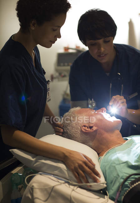 Женщина-врач осматривает пожилого пациента фонариком в отделении интенсивной терапии — стоковое фото