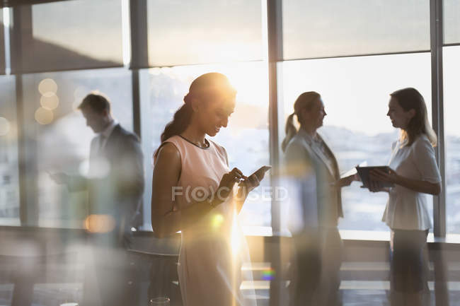Businesswoman texting with cell phone in sunny conference room — Stock Photo