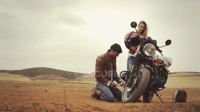 Young couple repairing motorcycle in remote countryside field — Stock Photo