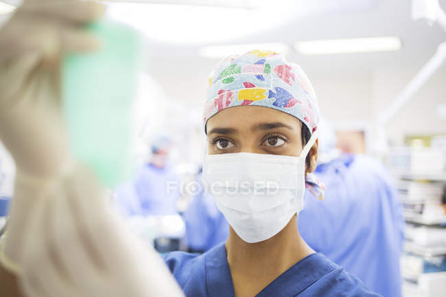 Maskierter Chirurg justiert Kochsalzbeutel während Operation — Stockfoto