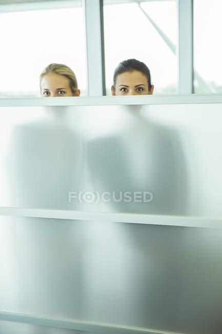 Деловые женщины подглядывают через половину стены в офисе — стоковое фото