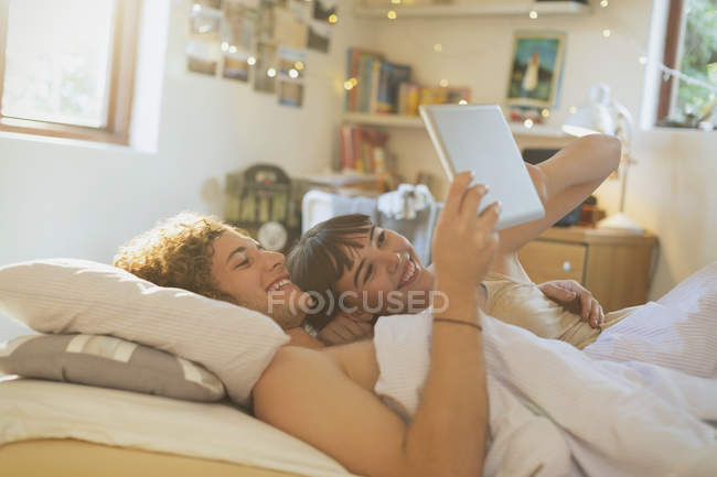 Lächelndes junges Paar liegt mit digitalem Tablet im Bett — Stockfoto