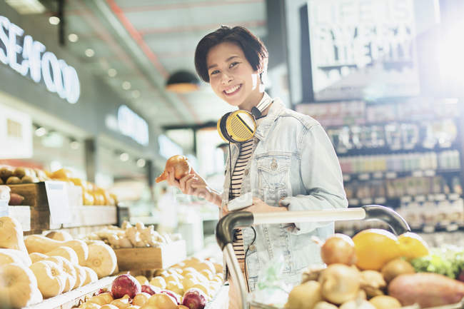 Portrait souriant jeune femme avec écouteurs épicerie shopping dans le marché — Photo de stock