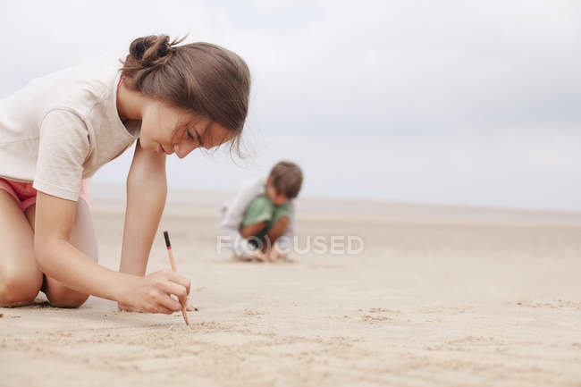 Menina com vara escrevendo na areia na praia de verão — Fotografia de Stock