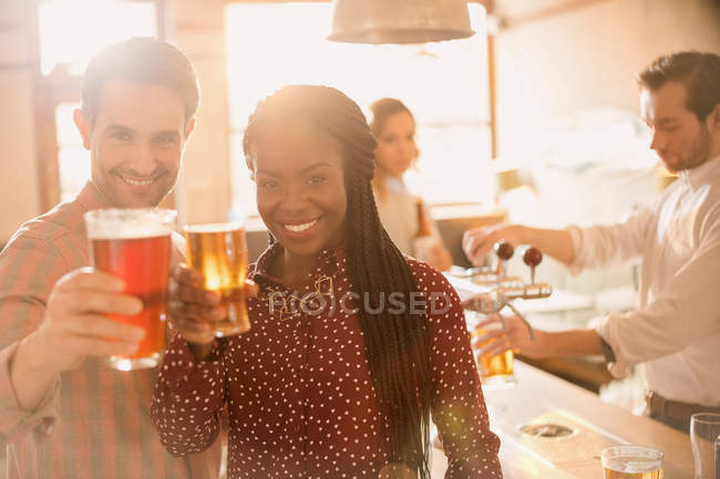Retrato sorrindo casal brindando copos de cerveja no bar — Fotografia de Stock