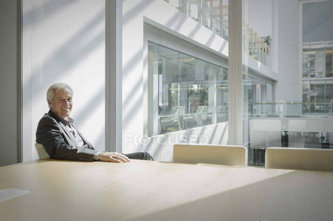 Retrato sorridente empresário sênior na sala de conferências ensolarada — Fotografia de Stock