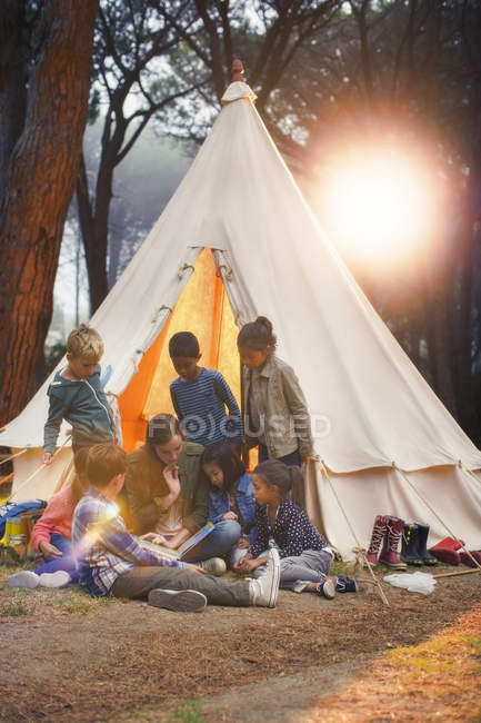 Students and teacher reading at teepee at campsite — Stock Photo