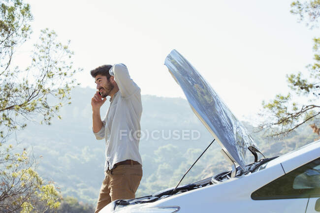 Man talking on cell phone with automobile hood raised at roadside — Stock Photo