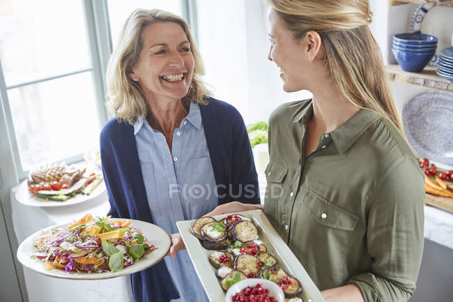 Sonrientes madre e hija sirviendo comida - foto de stock