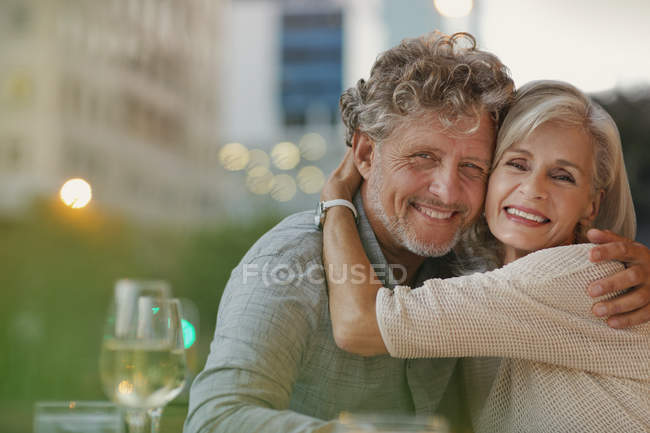 Portrait smiling senior couple hugging at urban sidewalk cafe — Stock Photo