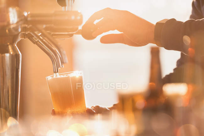 Close up male bartender pouring pint of beer from beer tap behind bar — Stock Photo