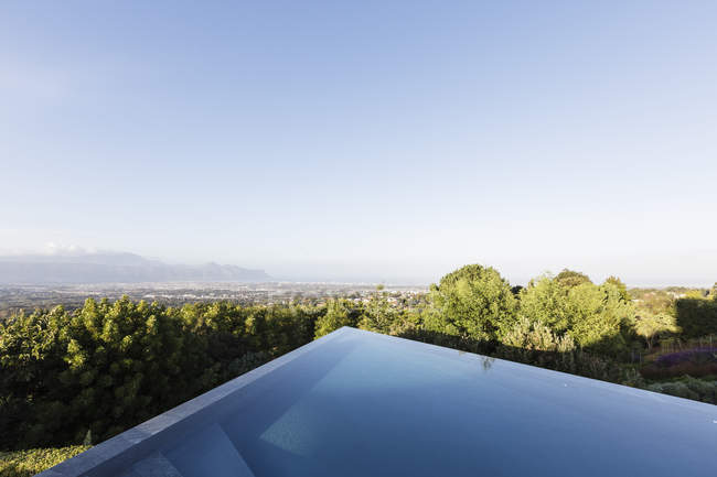 Moderne, piscine à débordement géométrique avec vue ensoleillée sous le ciel bleu — Photo de stock
