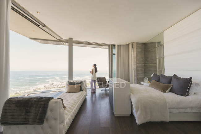 Mulher olhando para a vista do mar a partir de casa de luxo moderno vitrine quarto — Fotografia de Stock