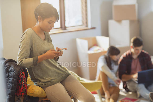 Mujer joven mensajes de texto con teléfono celular en nuevo apartamento - foto de stock