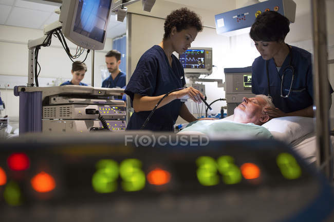 Médicos que atendem pacientes em unidade de terapia intensiva, equipamentos de monitoramento em primeiro plano — Fotografia de Stock