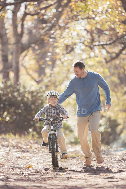 Father teaching son to ride a bicycle on path in woods — Stock Photo