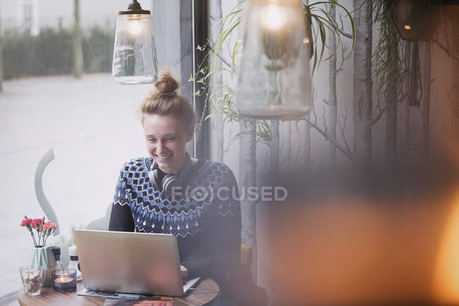 Sorrindo jovem mulher usando laptop na janela do café — Fotografia de Stock