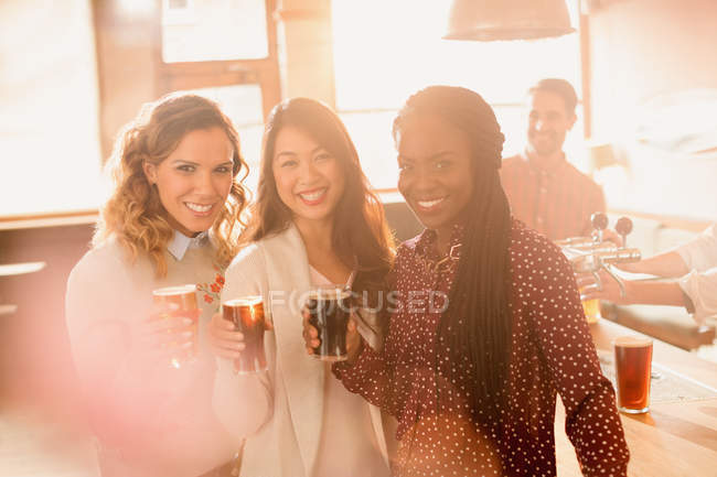 Retrato sonriente mujeres amigos bebiendo cerveza en el bar - foto de stock