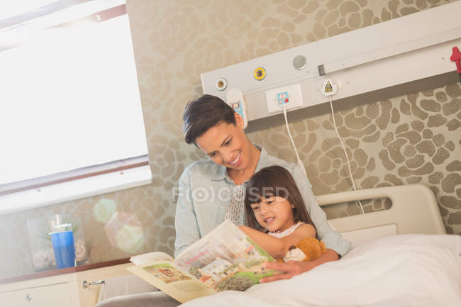 Mother reading book with daughter patient in hospital room — Stock Photo