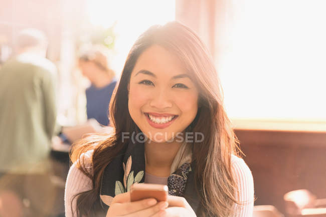 Retrato sonriente mujer china mensajes de texto con teléfono celular en la cafetería - foto de stock