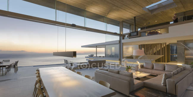 Moderno, casa de lujo escaparate sala de estar y comedor abierto a la vista al mar al atardecer - foto de stock