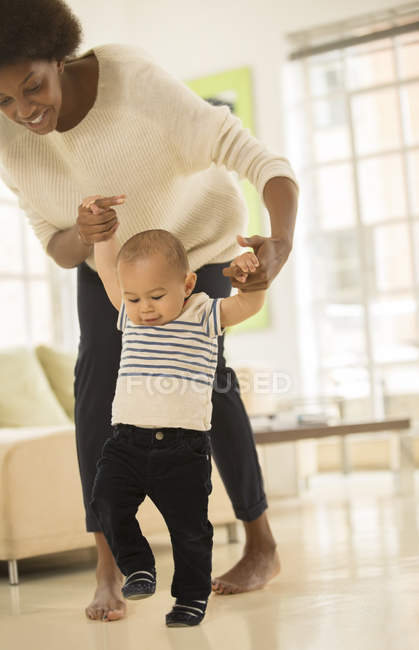 Mother helping baby boy walk in living room at home — Stock Photo