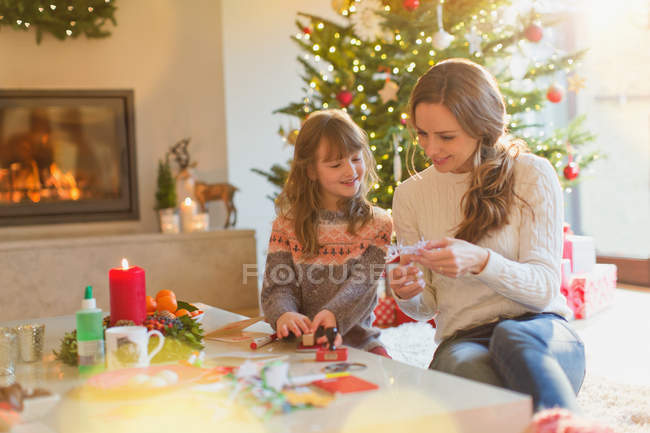 Madre e hija haciendo decoraciones de copos de nieve de Navidad en la sala de estar - foto de stock