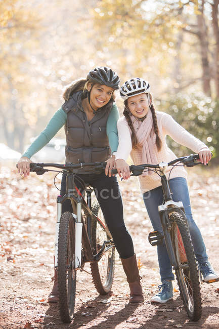 Retrato sonriente madre e hija en bicicletas de montaña en el bosque - foto de stock