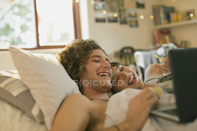 Sorrindo jovem casal deitado na cama usando laptop — Fotografia de Stock