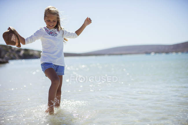 Jeune fille éclaboussant dans l'eau sur la plage — Photo de stock