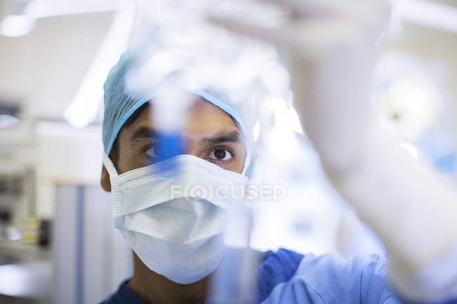 Surgeon wearing surgical mask, cap and gloves looking closely at IV drip — Stock Photo