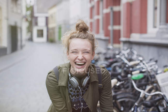 Portrait enthusiastic, laughing young woman with headphones on city street — Stock Photo