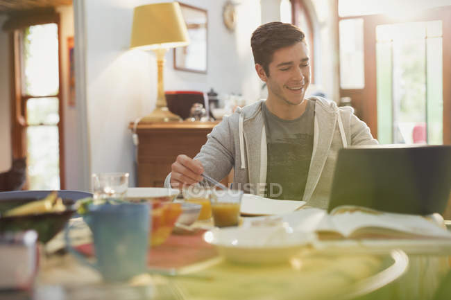 Молодий студент коледжу використовує ноутбук, який навчається на сніданку — стокове фото