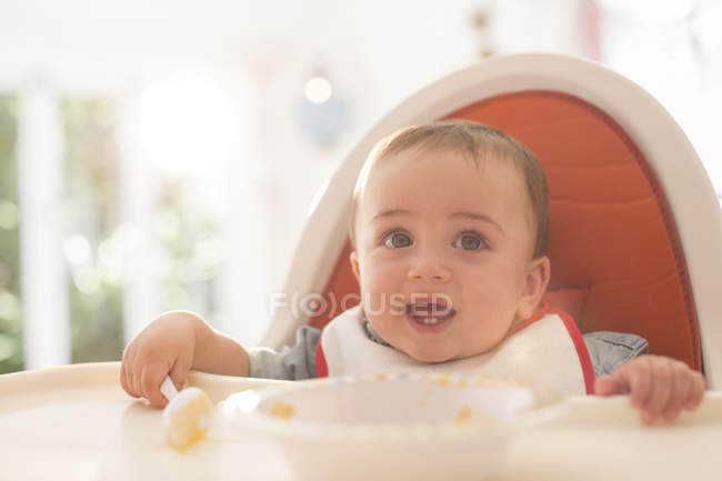 Baby boy eating in high chair — Stock Photo