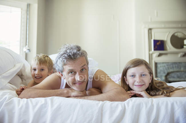 Pai e filhos relaxando na cama — Fotografia de Stock