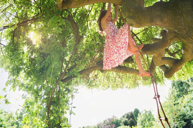 Mädchen im Sonnenkleid klettert auf Baum — Stockfoto